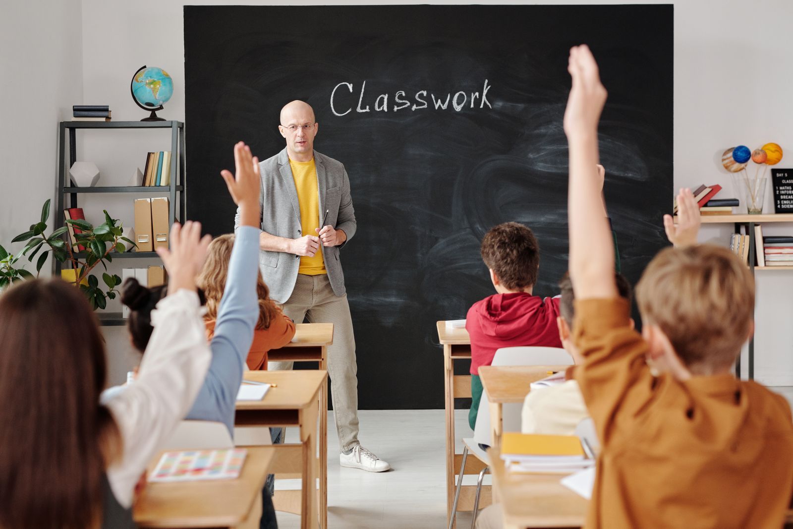 Učitel před tabulí a žáci s rukama nahoře ve třídě