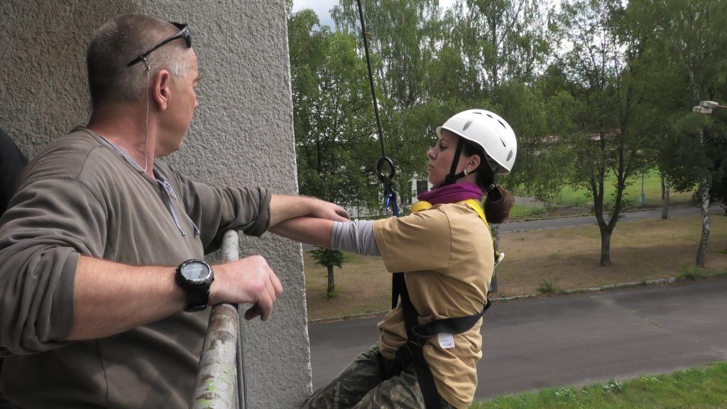 Instruktor připravuje cvičence ke slaňování z budovy